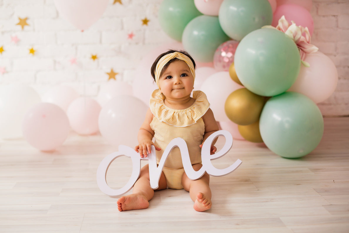 a 12 month old baby in a yellow outfit holds a sign that says