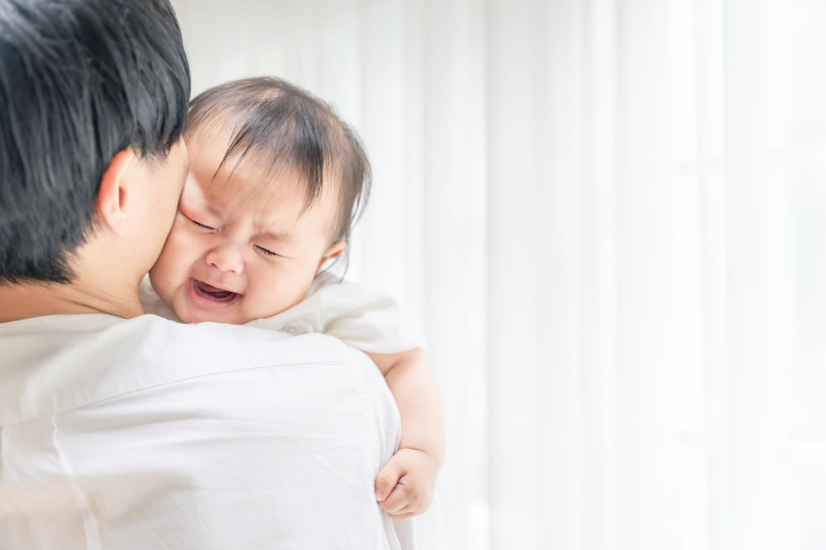 a 4 month old baby cries on their dad's shoulder as he comforts the baby.