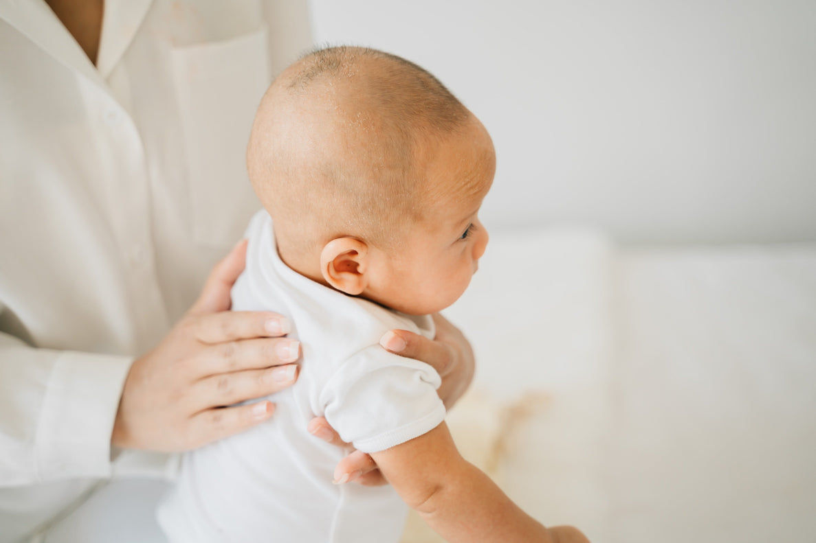 a young baby is sat on an adults lap as the adult tries to burp them gently with their hand on the baby's back