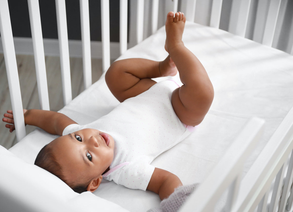 a baby lays in a crib with his legs in the air playfully