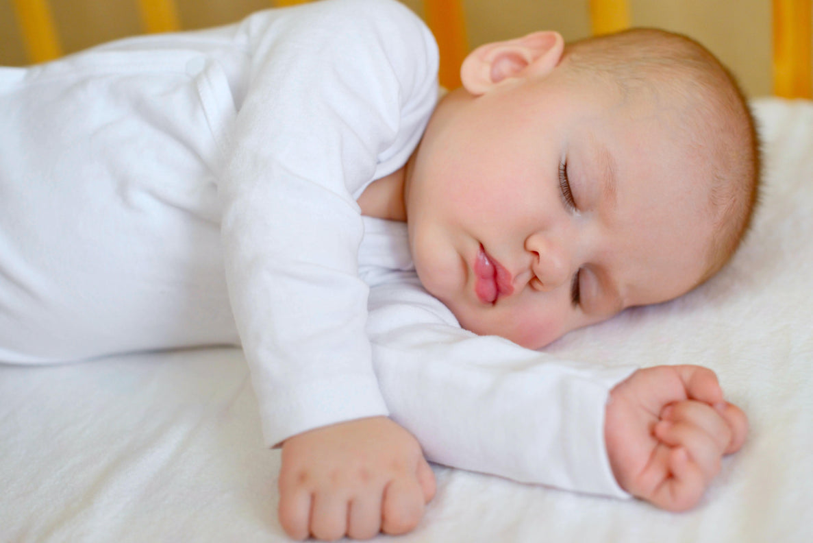 a baby is asleep laying on their side with arms outstretched in a crib