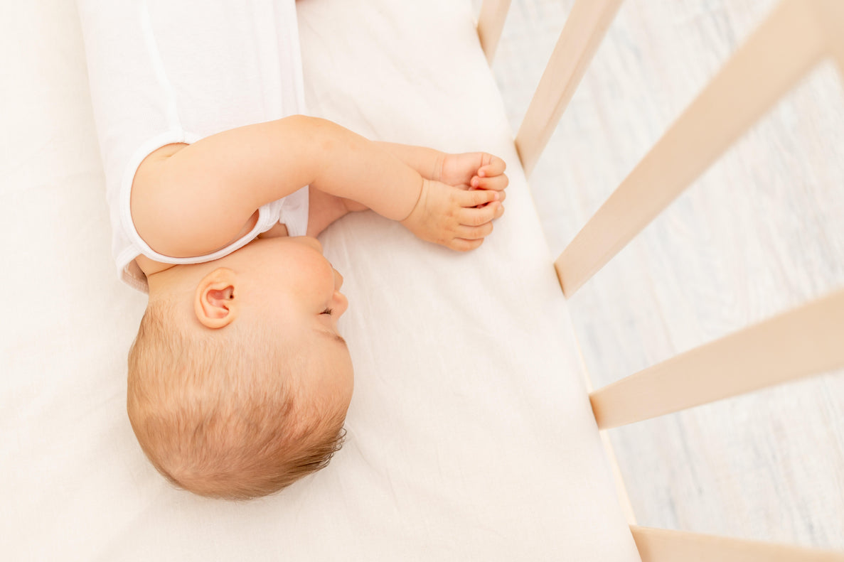 a baby lays on their side sleeping in a light colored crib on a light colored sheet