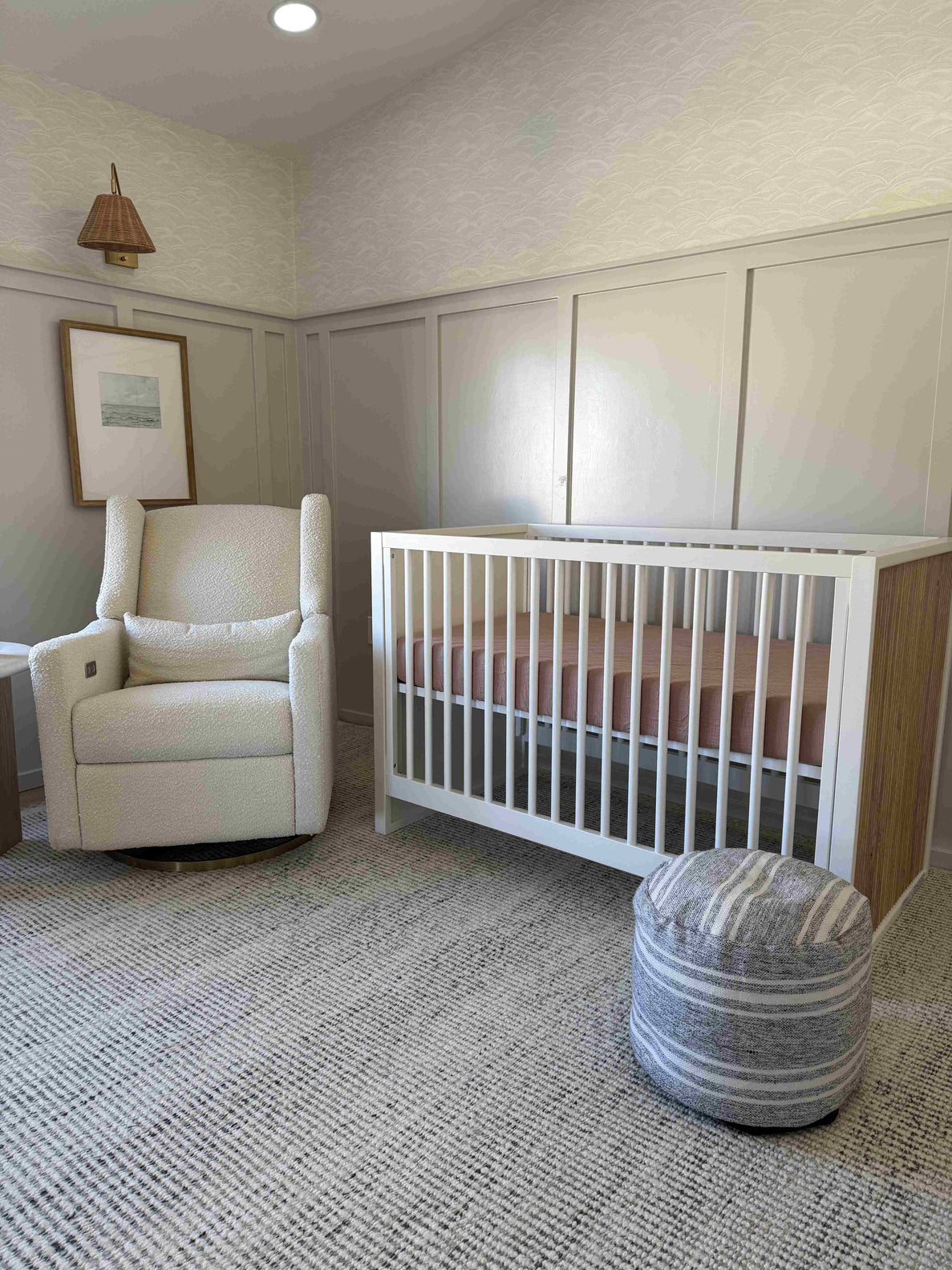 a photo shows a nursery set up with a white rocking chair, white crib, and striped ottoman