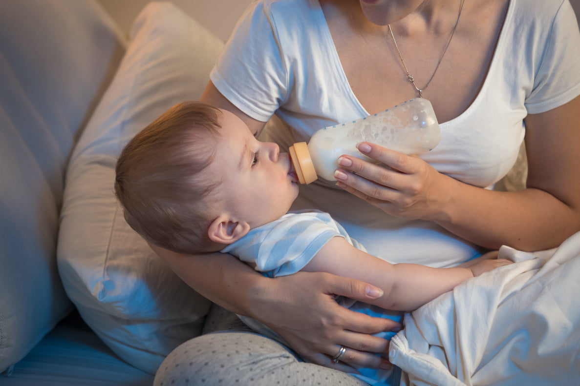 A closeup of a woman feeding a baby with a bottle as she holds him in her lap.
