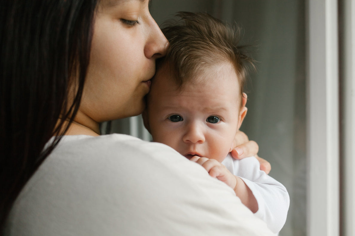 A mom kisses her newborn's head as she holds them up on her shoulder