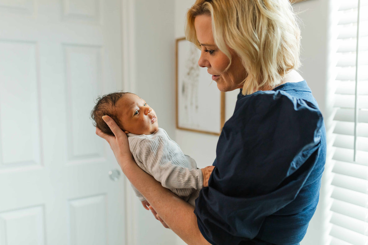 a woman holds a newborn at arms length observing sleepy cues
