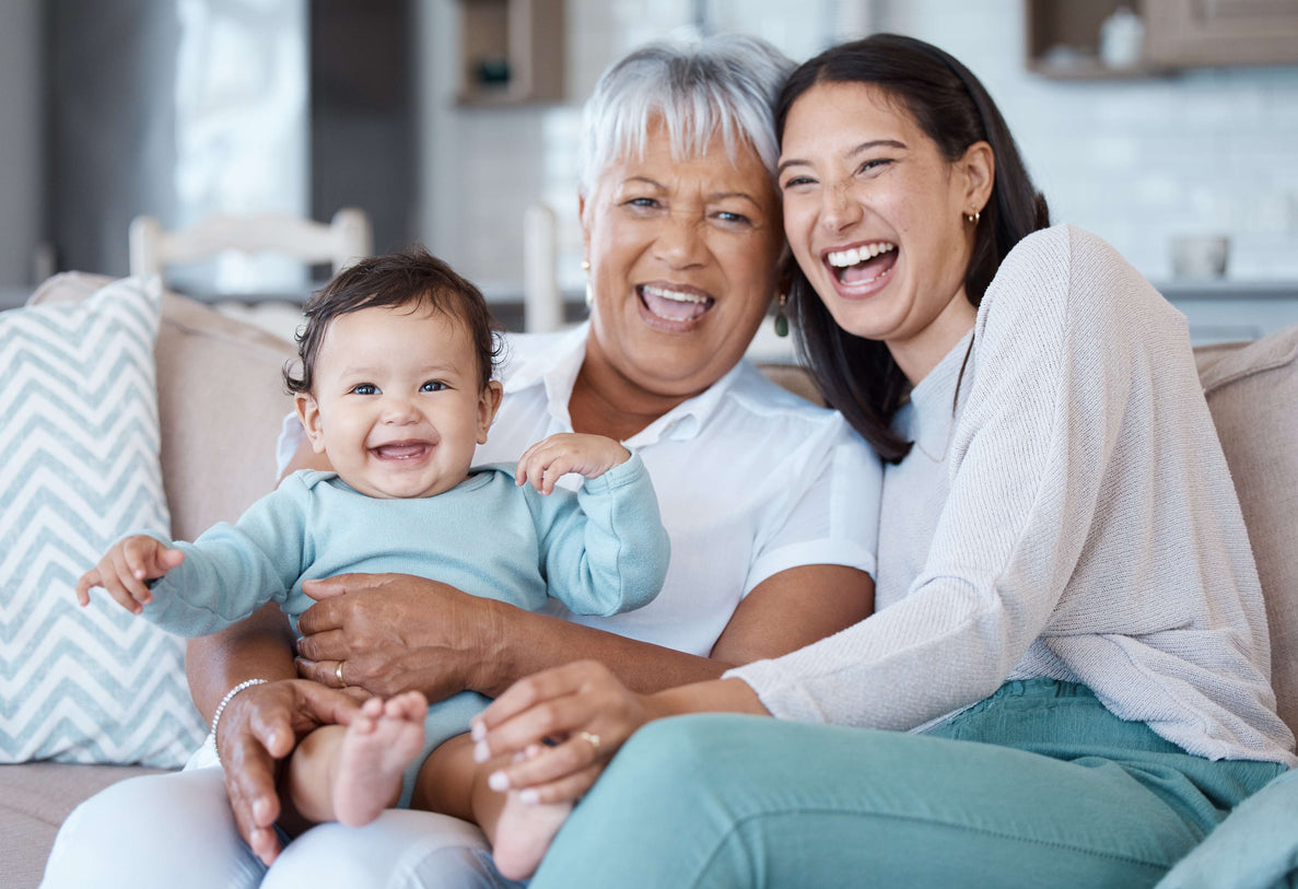 a photo of a mom, grandma, and baby all snuggling on a couch smiling and laughing