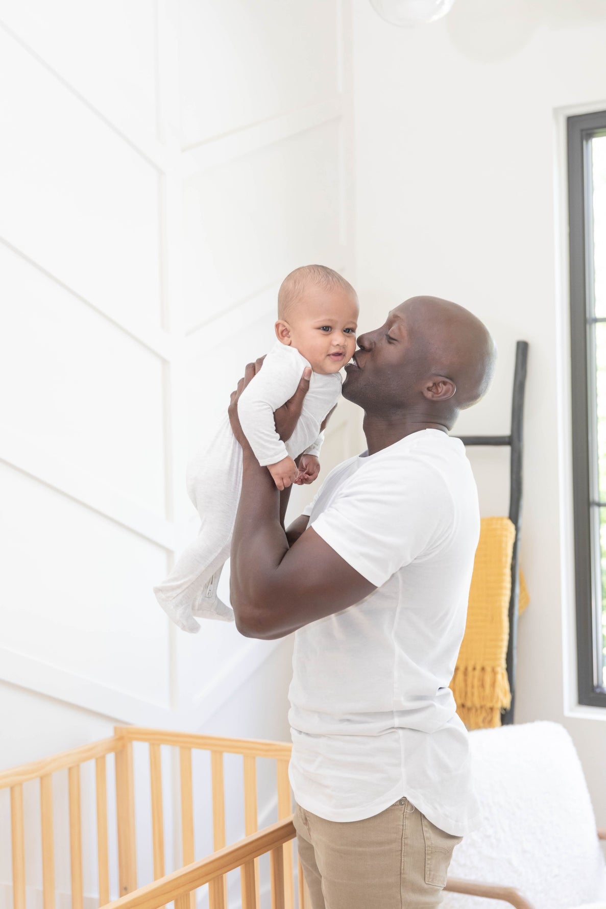 A dad holds his baby up to him with 2 hands to kiss him before placing him in his crib