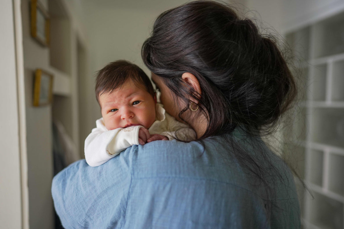a dark haired mom holds a dark haired newborn over her arm. The newborn looks sleepy