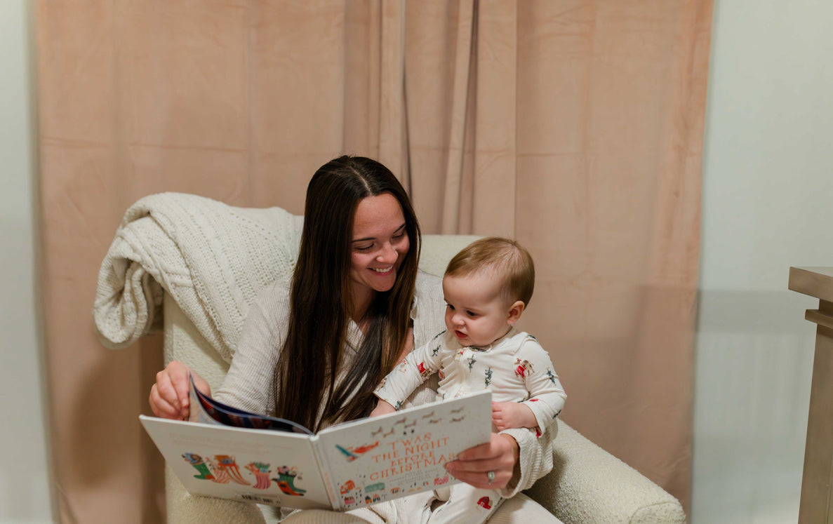 10 month old sitting on mom's lap reading a book 