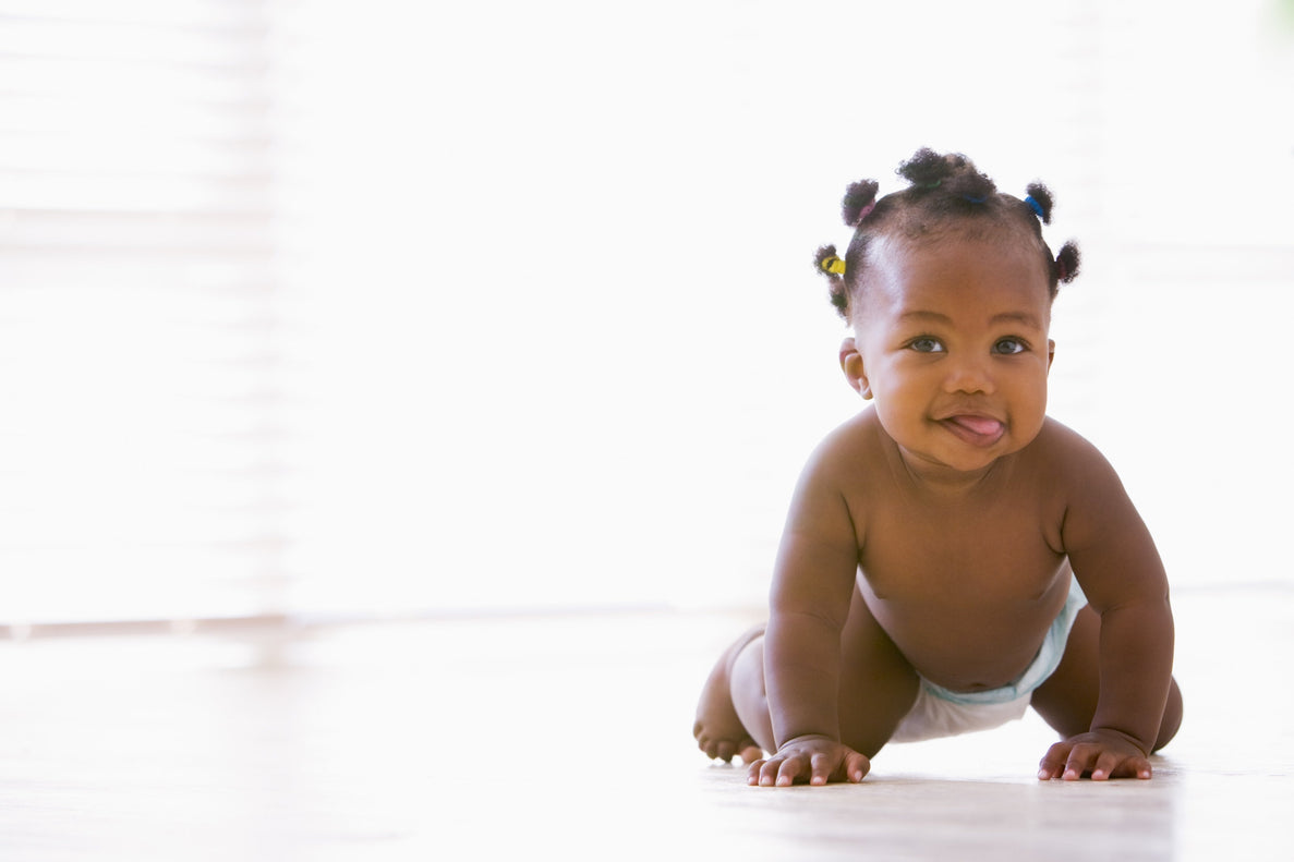 a 10 month old baby in a diaper crawls towards the camera sticking out their tongue