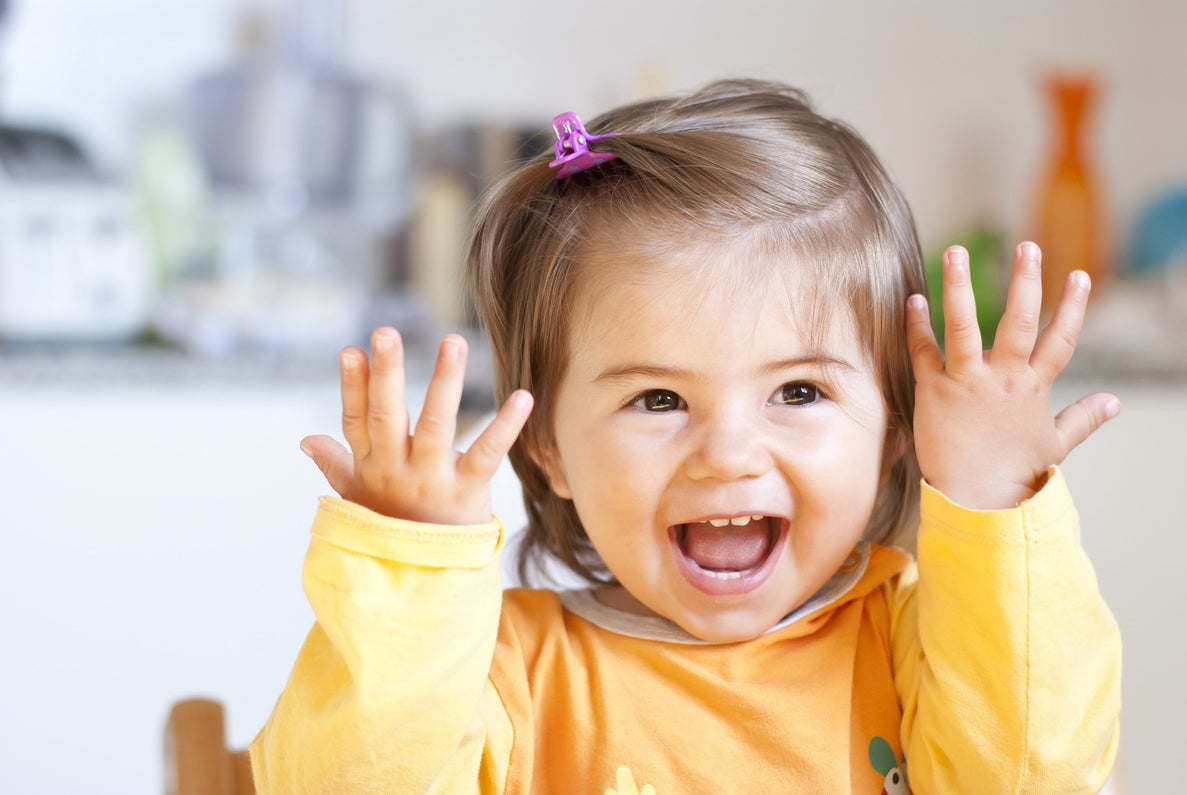 a 20 month old baby wearing an orange shirt smiling and holding her hands up in excitement