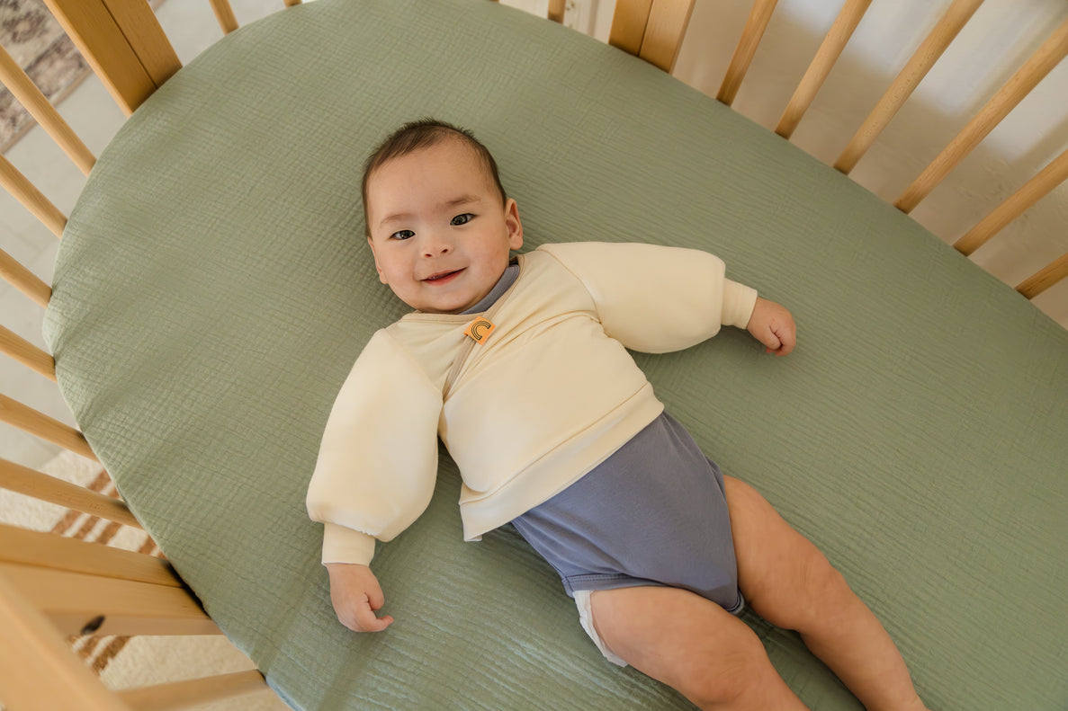 baby laying in crib looking at camera wearing Jacky, the swaddle transition jacket