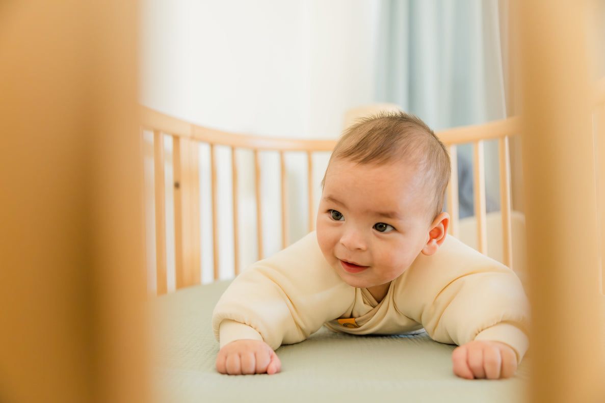 baby on tummy wearing Jacky, the swaddle transition jacket, in crib