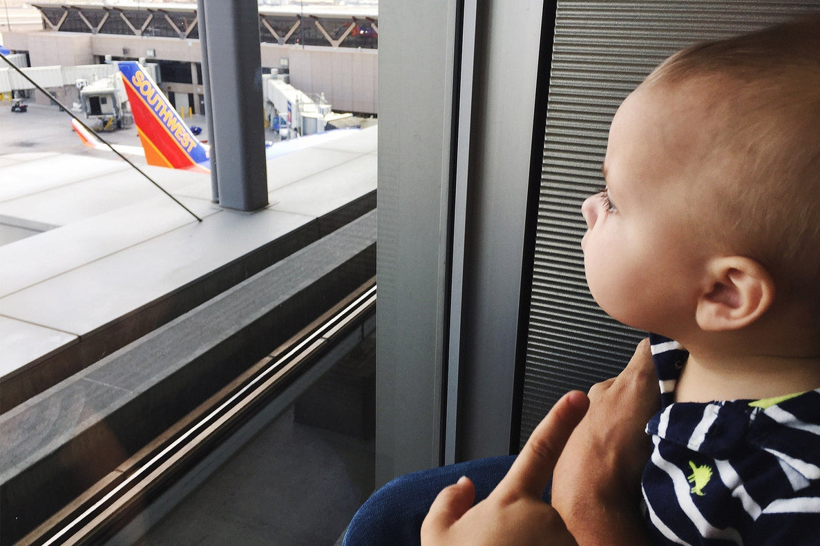 a baby looks out the window at an airport. Planes are shown in the background