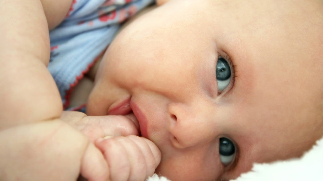 A closeup of a baby's face as they suck their thumb laying on their side