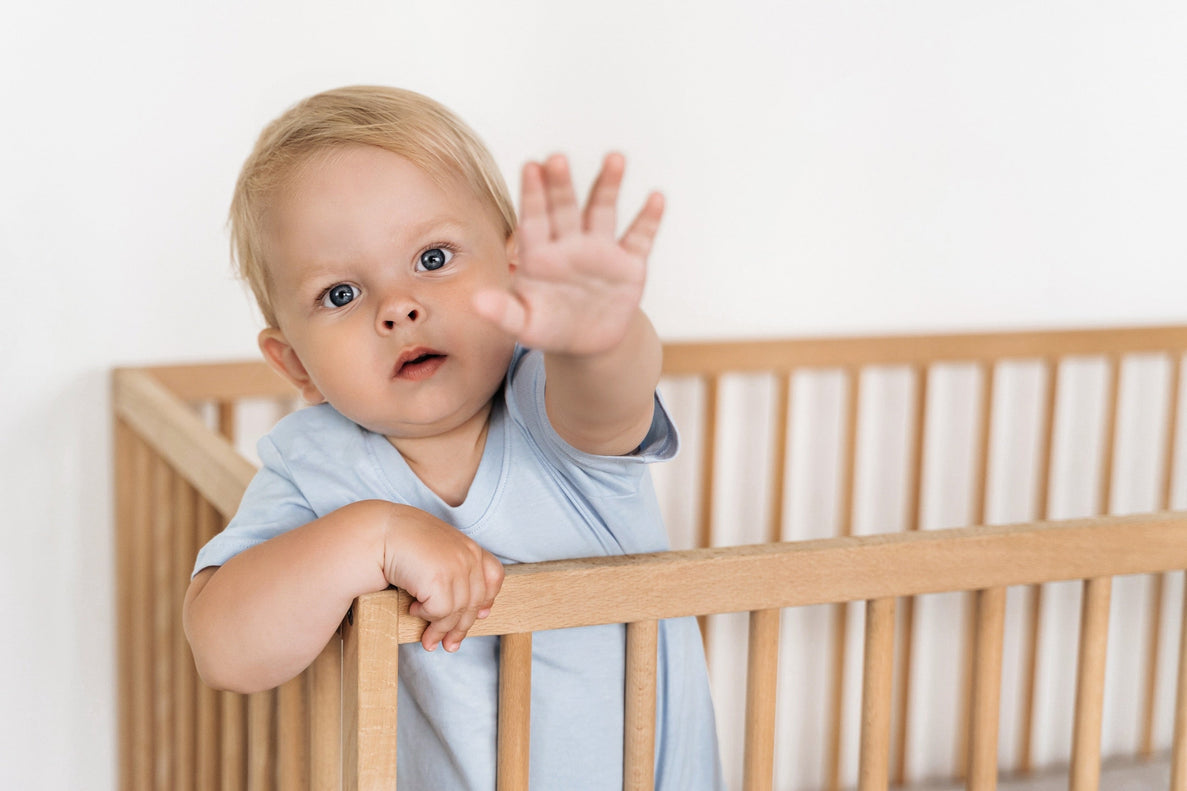 a baby stands in his crib reaching for the camera