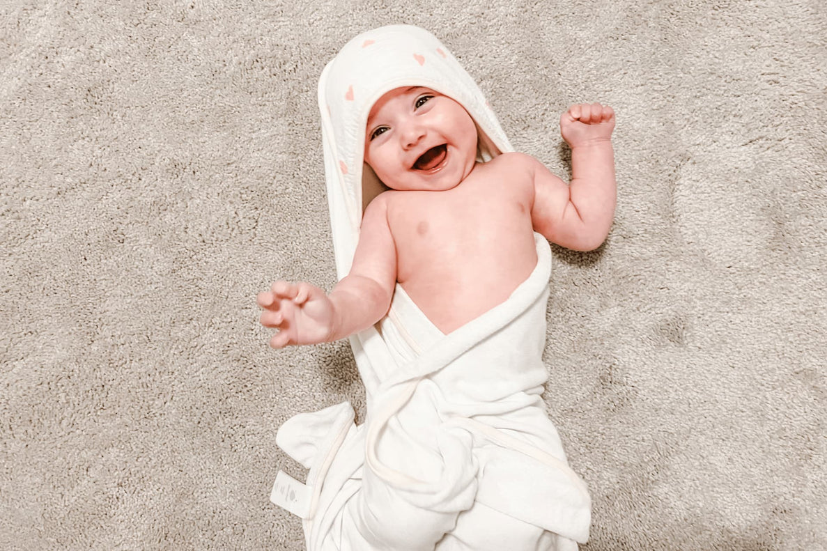 a happy looking baby is wrapped in a white towel with a hood laying on top of a beige rug