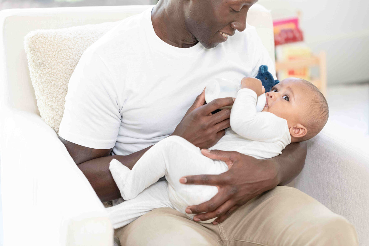 a dad looks fondly at his baby cradling them in his arms and feeding a bottle. 