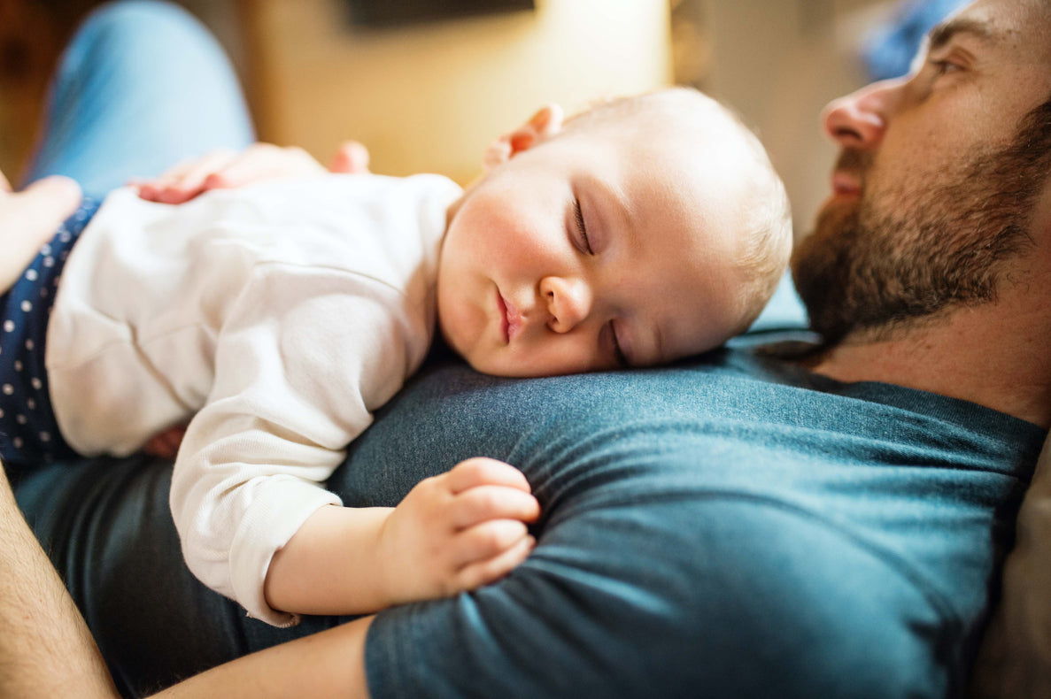 a closeup of a baby sleeping on dad's chest. Dad looks relaxed and has his hand on the baby's back for comfort. 