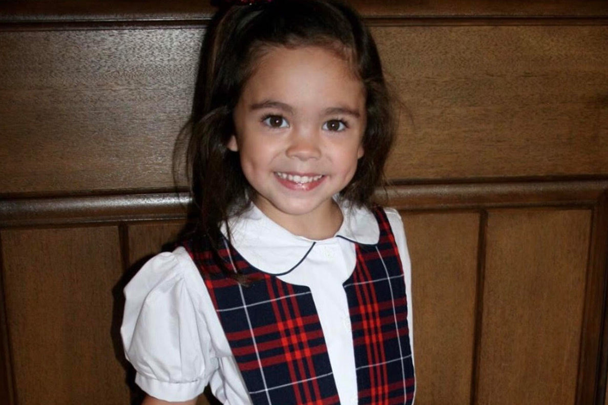 a picture of a young school-aged girl wearing a uniform and white blouse smiles at the camera