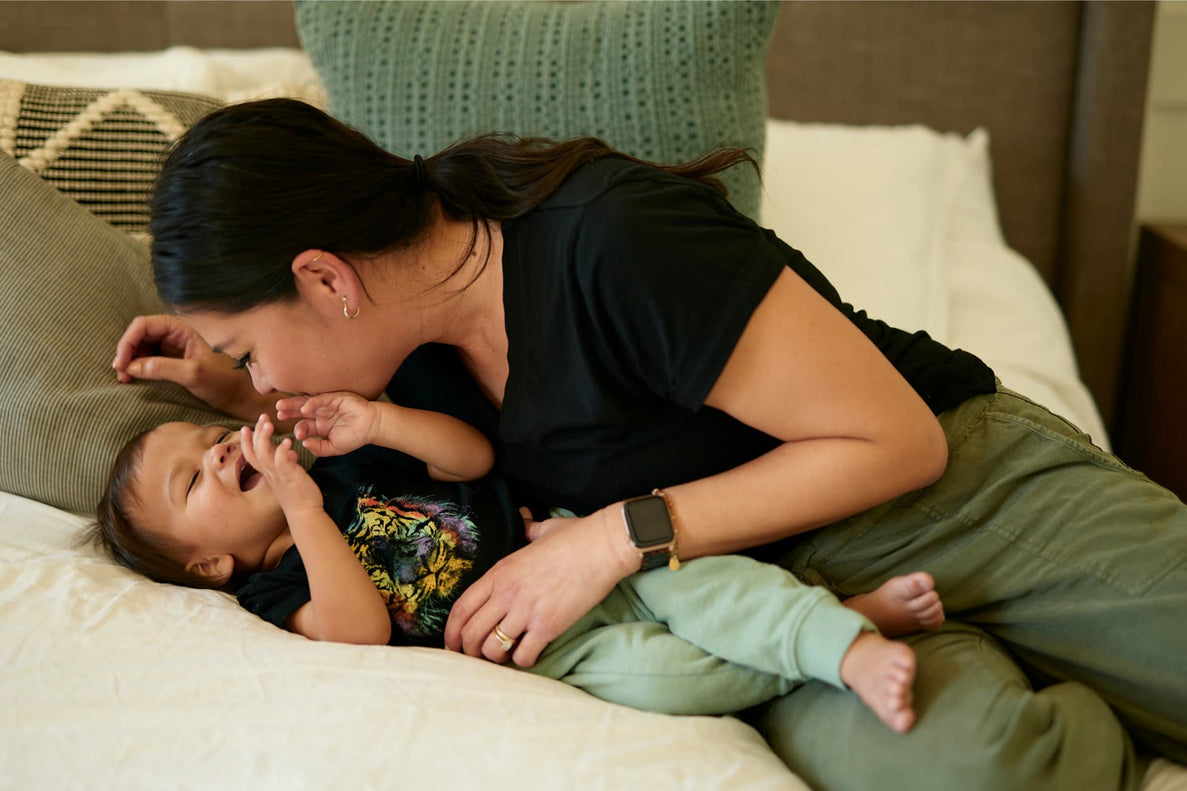 a mom and son play together and snuggle on a bed with colorful pillows in the background