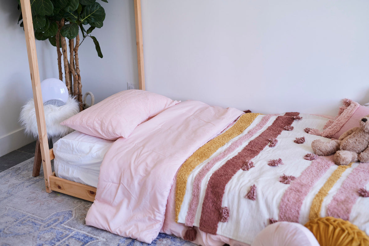 An image of a child's montessori floor bed with pink, yellow, and burgundy colored bedding
