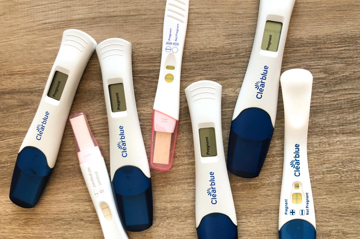 A closeup of 7 pregnancy tests lay on top of a wooden surface