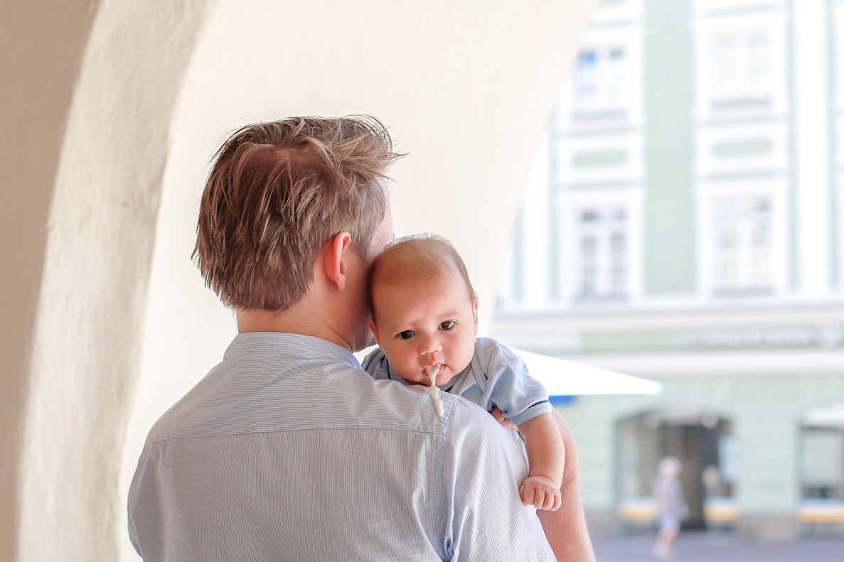 A dad holds a baby over his shoulder. The baby is spitting up on his shoulder 