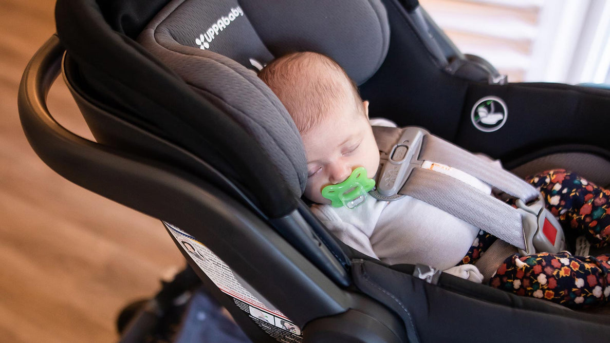 a closeup image of a small baby sleeping in a car seat with a green pacifier in their mouth
