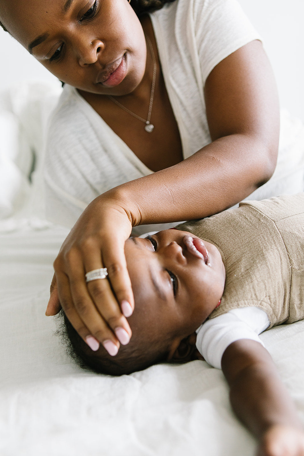 a mom with a concerned expression puts her hand on baby's forehead. Baby looks unhappy