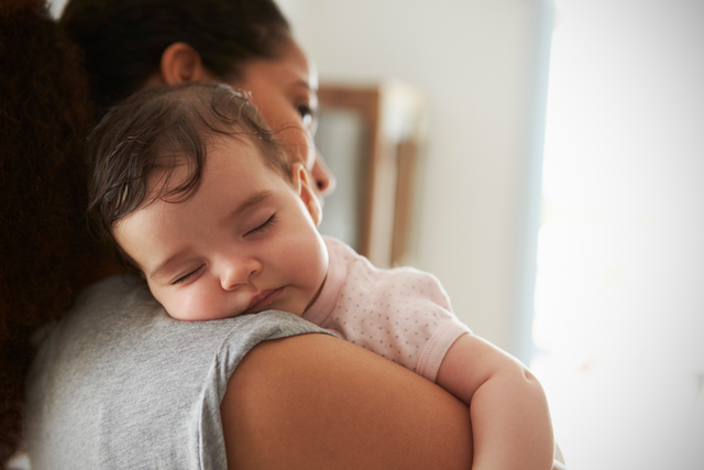 A baby is sound asleep on her mother's shoulder