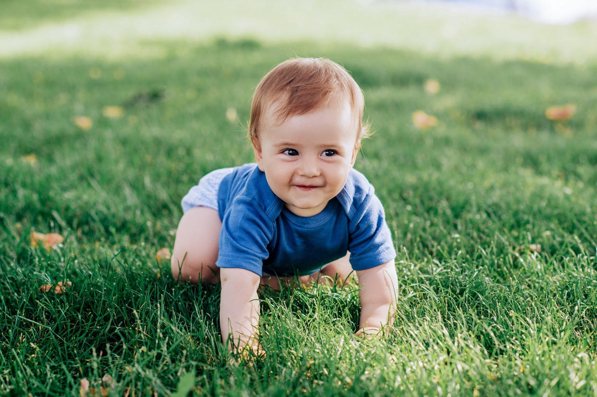 a smiling baby boy dressed in blue crawls through the grass