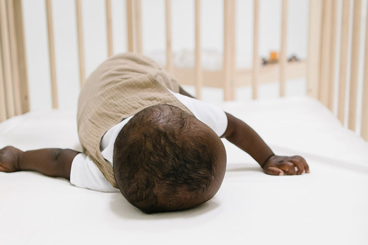 a baby lays on his tummy in a crib using his hands to push up and try to roll
