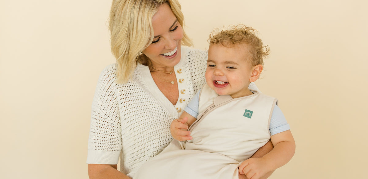 Cara Dumaplin holding a toddler in a Taking Cara Babies sleep sack